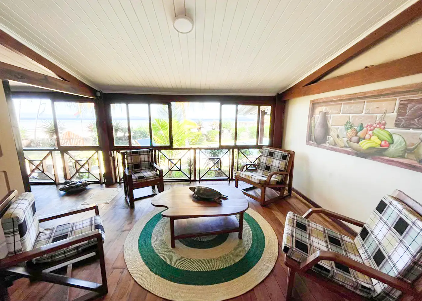 Cozy porch with plaid chairs, wooden coffee table with turtle sculpture, round rug, and tropical view.
